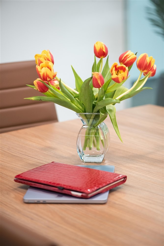 Red-and-yellow tulips in a vase with a red planner and laptop on a conference table.