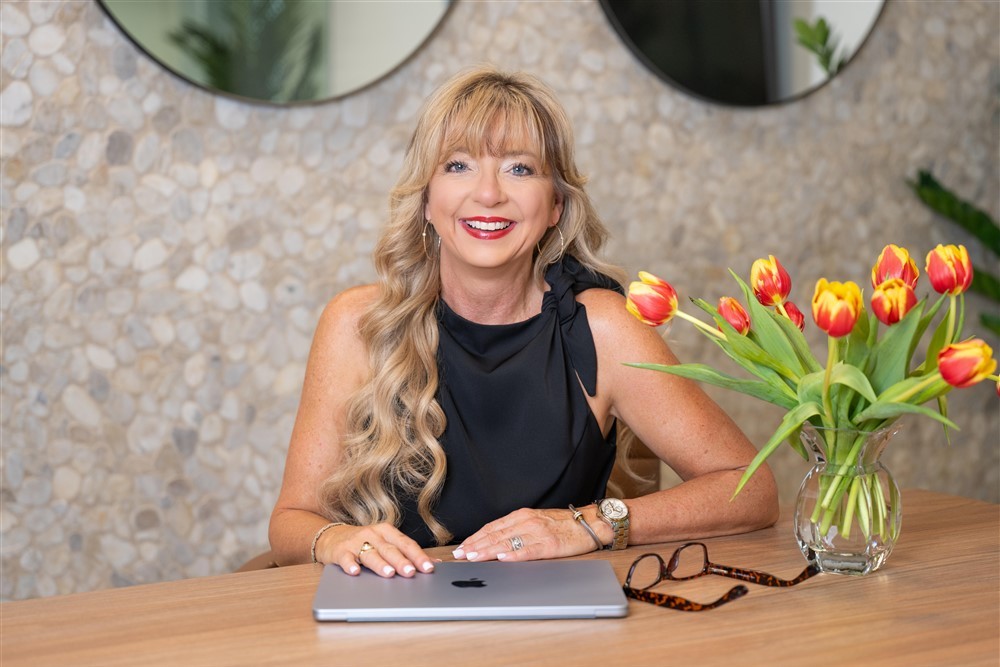 Stacy Harris smiling at a desk with a laptop and flowers.