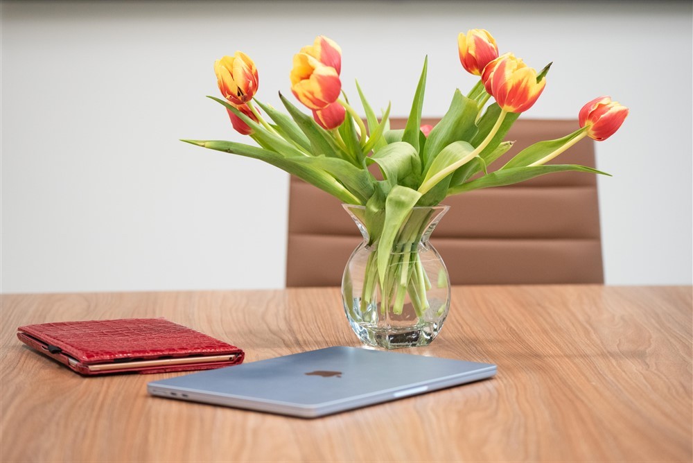 Red-and-yellow tulips, red planner and laptop arranged on a conference table.