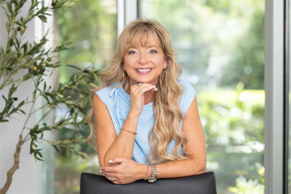 Stacy Harris smiling in a light blue top with a bright office background.