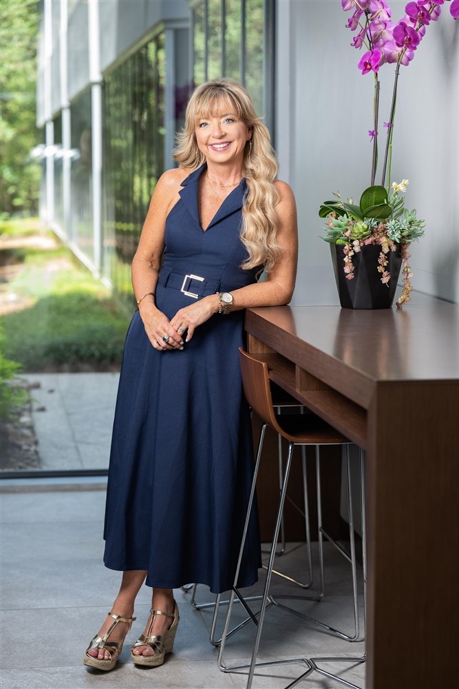Full-length portrait of Stacy Harris in a navy blue dress beside a table and orchid.