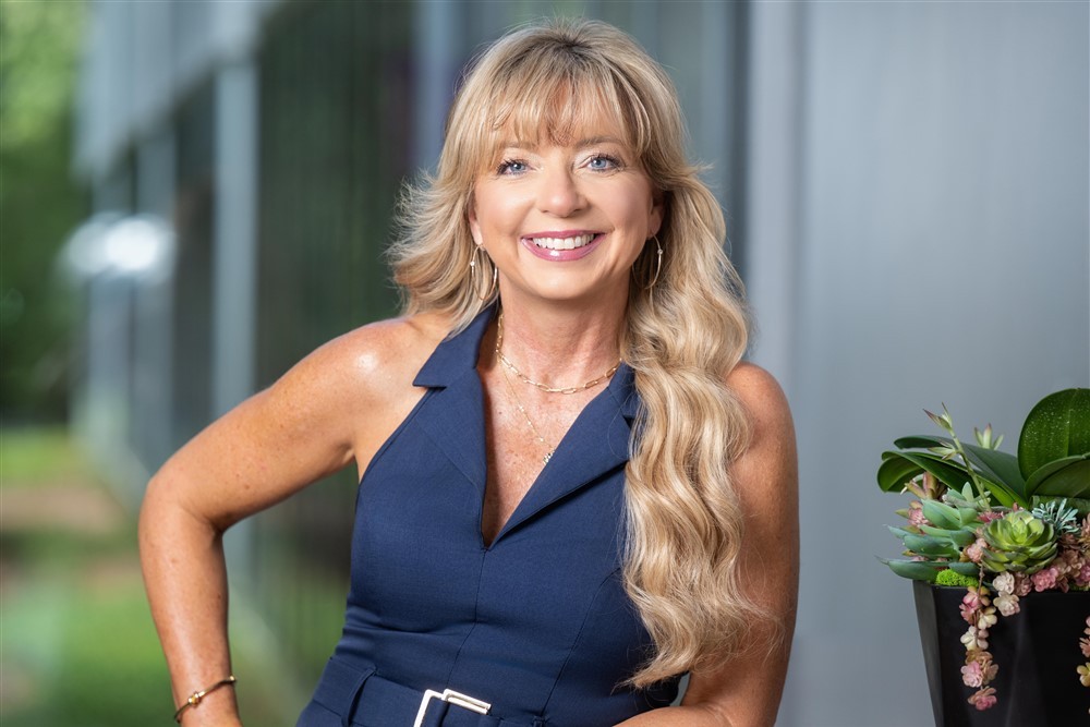 Stacy Harris smiling in a navy blue dress in a modern office setting.
